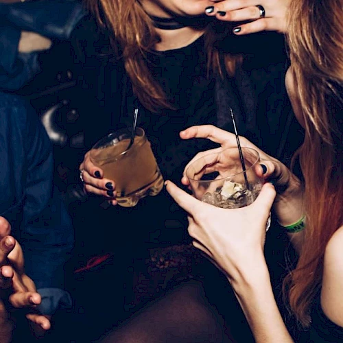 The image shows a group of people at a social event, holding drinks and engaging in conversation, with one person laughing.