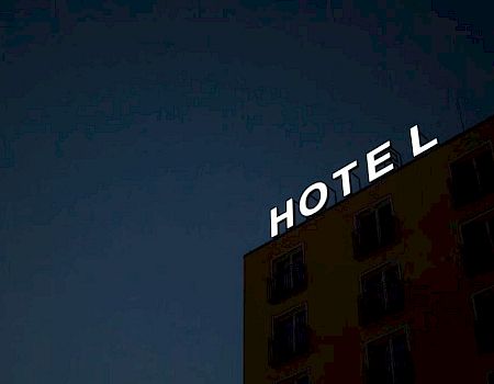 The image shows the facade of a building at night with the word "HOTEL" displayed prominently in illuminated letters.