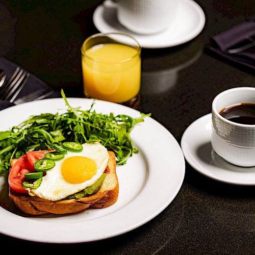 The image shows a breakfast setup with a plate containing an egg on toast, greens, a glass of orange juice, and a cup of coffee.