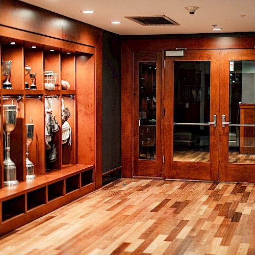 A wooden hallway with sports equipment on shelves, double glass doors, and a "Welcome to Victory" sign by the entrance ending the sentence.