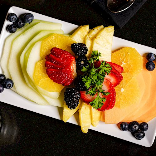 A rectangular plate with assorted fruits including strawberries, pineapple, melon, and berries, garnished with herbs.