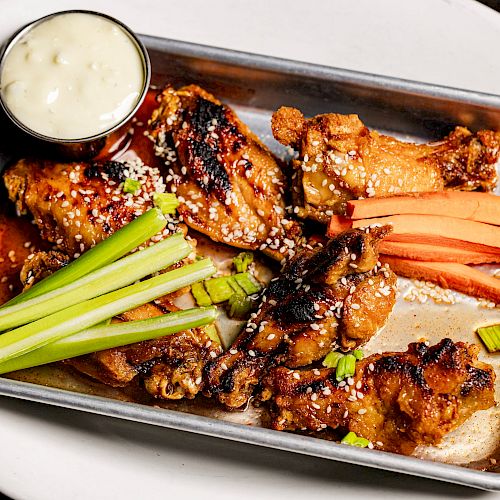 A tray with chicken wings, celery sticks, carrot sticks, and a small cup of dipping sauce on a white plate.