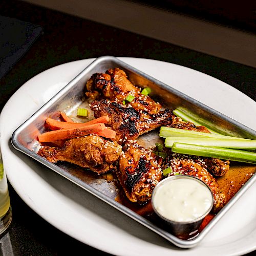 A tray with chicken wings, carrot sticks, celery sticks, and a cup of dipping sauce is placed on a white plate.