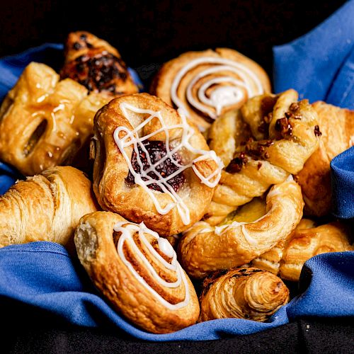 A variety of pastries are placed on a blue cloth, including croissants and danishes with icing and fillings ending the sentence.