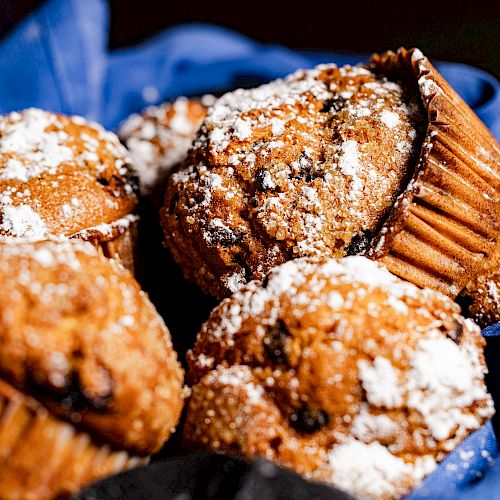 A basket of freshly baked muffins dusted with powdered sugar, resting on a blue cloth.