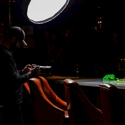 A person in a dark setting is taking a photo of a table with fruit and drinks under a bright overhead light, with bar chairs visible.