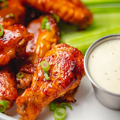 A plate of buffalo wings garnished with green onions, served with celery sticks and a side of ranch dipping sauce.